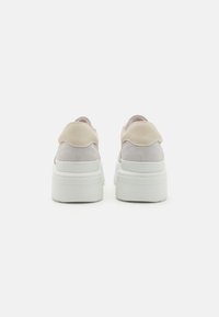 Sko laget av myk semsket skinn i lys grå og beige, med en kraftig hvit plattformsåle og rund bakdesign.