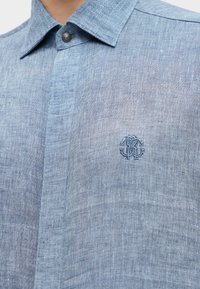 Ανοιχτό μπλε πουκάμισο από λινό με γιακά που κουμπώνει και μικρό κεντημένο λογότυπο στο στήθος.