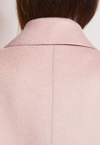 Rosa strukturierter Mantel mit einer weichen, taktilen Oberfläche, ausgestattet mit einem Rückenkollor und Nahtdetails; von hinten betrachtet.