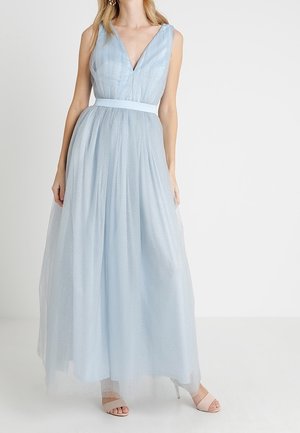 Femme portant une robe longue sans manches bleu clair avec un décolleté en V et une taille cintrée, associée à des talons ouverts.