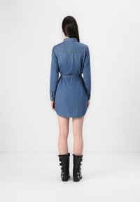 Robe chemise en denim avec des manches longues, taille ceinture, ourlet arrondi et couleur bleu clair. Associée à des bottes noires montantes avec des boucles.