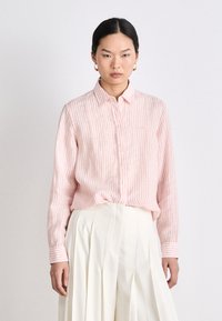 Light pink striped button-up shirt with a collar and long sleeves. Features vertical stripes and subtle textured fabric. Paired with a white pleated skirt.