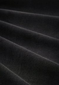 Glat sort stof med bløde folder, der skaber horisontale skyggefulde linjer på tværs af overfladen.