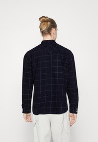 Marinblå flanellskjorta med ett vitt rutmönster, med spetsig krage och långa ärmar, knäppta manschetter och rak fåll.