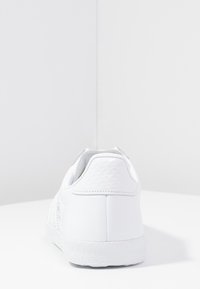 Vita sneakers med texturerad bakpanel, slät läderöverdel, gummisula och sömnadsdetaljer. Minimalistisk design och rundad form.