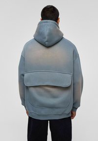 Blauwe hoodie met een ruime achterzak, een gladde textuur en een lichte kleurverloop van donker naar licht.