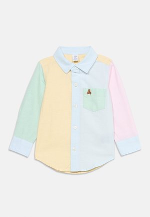 Chemise boutonnée à manches longues avec des panneaux en bloc de couleur jaune pastel, vert, bleu et rose, comportant une poche poitrine avec un petit patch ours en peluche.