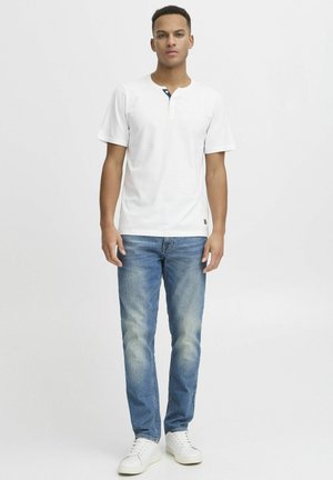 Chemise henley blanche à manches courtes avec une patte de boutonnage navy, associée à un jean bleu clair et des baskets blanches. Coup simple et décontracté.
