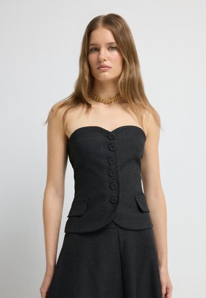 Haut noir sans manches en tissu texturé, présentant six grands boutons, deux poches latérales et une coupe ajustée, associé à une jupe assortie.