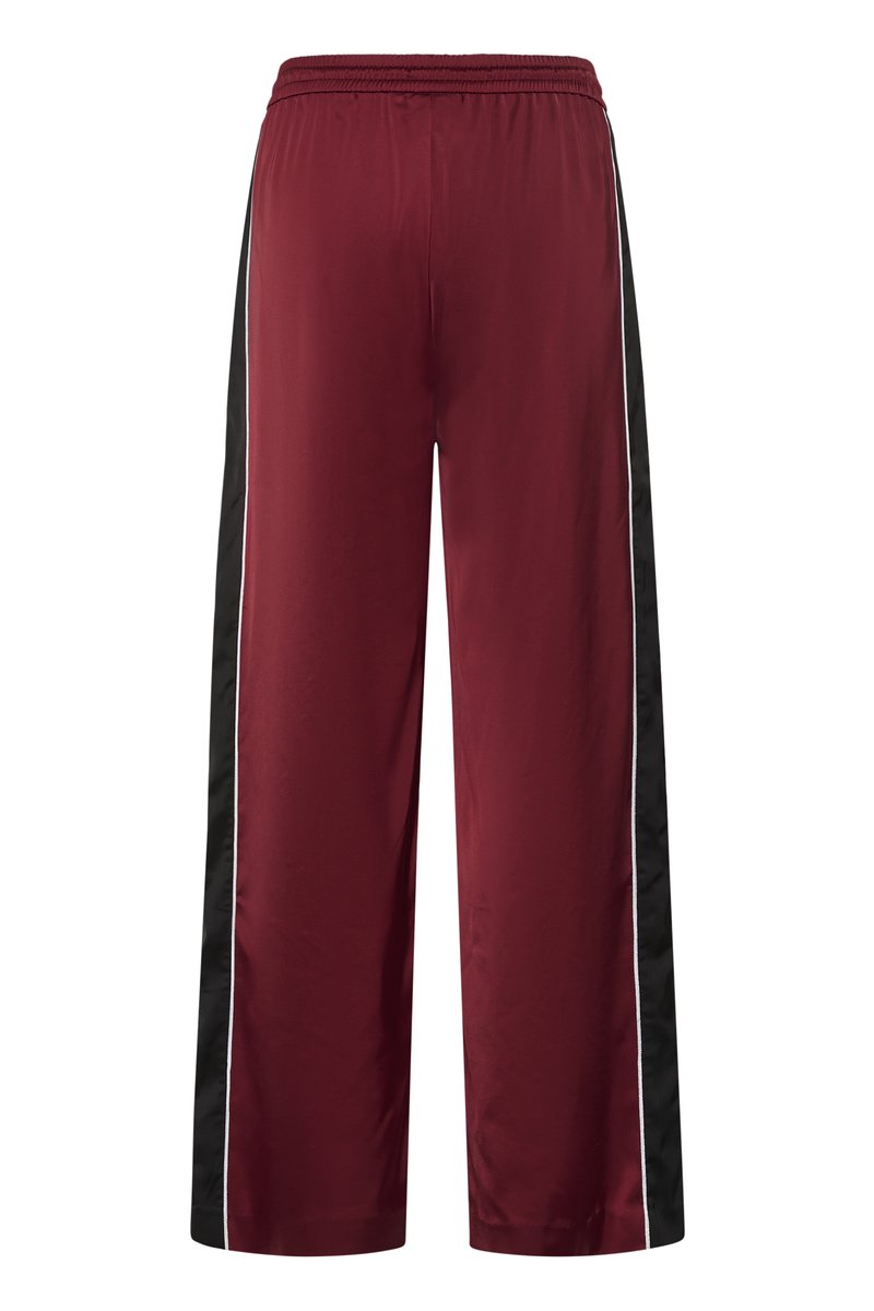 Pantalon bordeaux à jambes larges avec taille élastique, panneaux latéraux noirs et fines bandes blanches le long des coutures latérales.