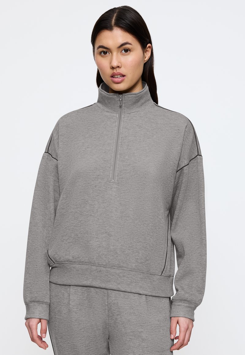 Felpa grigia con zip e colletto alto, vestibilità larga, maniche lunghe e polsini a coste; abbinata a pantaloni coordinati.