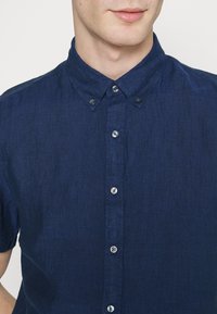 Camicia button-up a maniche corte di un blu navy scuro, realizzata in un tessuto testurizzato, con colletto, cuciture sottili e bottoni argentati.