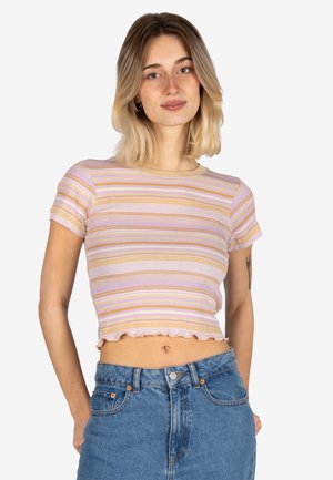 Junge Frau mit schulterlangem blondem Haar, die ein kurzes gestreiftes pastellfarbenes T-Shirt und hoch taillierte blaue Jeans trägt, mit den Händen in den Taschen.