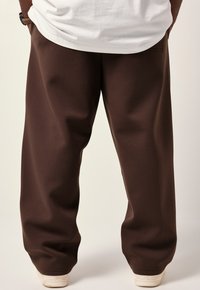 Bruine wijde benen broek van zacht stof, met een gladde textuur en een elastische tailleband, gecombineerd met witte lage sneakers.