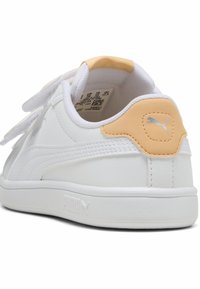 Fehér sneaker sima bőr felsőrésszel, narancs színű részletek a sarkán és tépőzáras pántokkal. Textúrázott részlet a talp közelében és márkajelzés az oldalon.