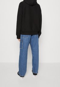 Černá mikina s kapucí a volnějším střihem, doplněná světlomodrými denimovými cargo kalhotami s bočními kapsami. Outfit je dokončen černými teniskami.