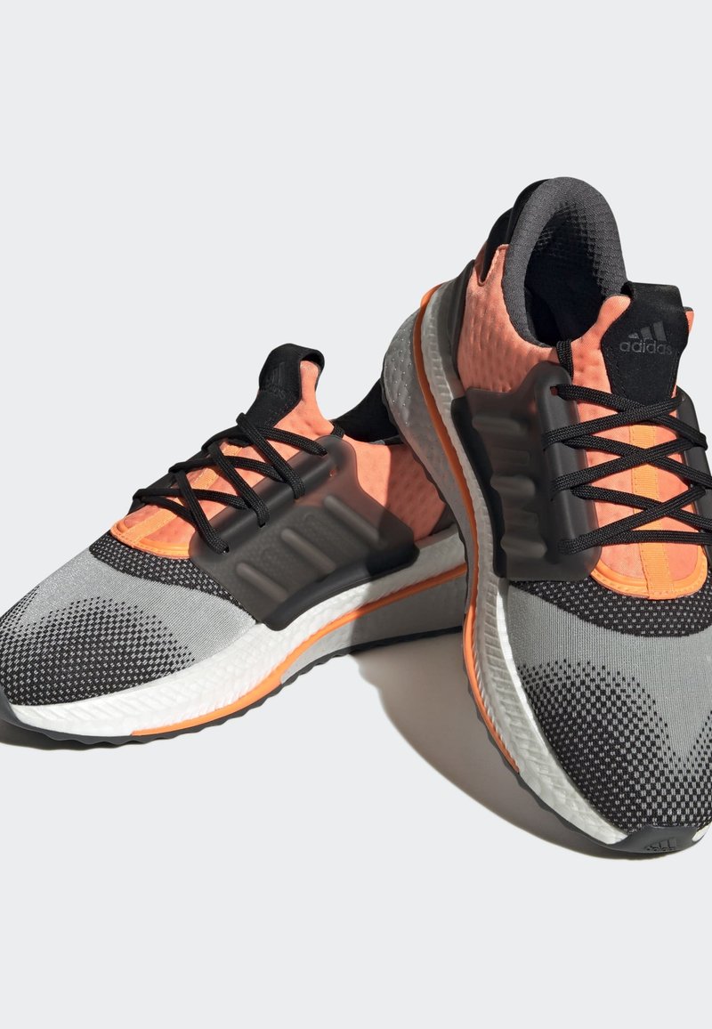 Zapatillas deportivas con una parte superior de malla transpirable en negro y rosa, superposiciones texturizadas en gris y una suela blanca acolchada con un acento naranja.