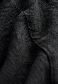 Tessuto nero testurizzato con un motivo intrecciato, mostrando linee morbide e lisce e una leggera lucentezza, disposto in modo da evidenziare contorni e profondità.