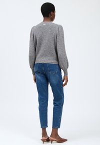 Maglione grigio a maglia con maniche a sbuffo, vita aderente e colletto rotondo, abbinato a jeans denim blu e mule marroni.