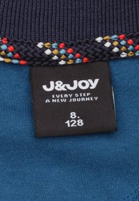 Marine gebreide stof met een meerkleurige gevlochten rand. Zwarte label met "J&JOY" en witte tekst die de maten aangeeft: "8" en "128."