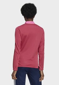 Camiseta deportiva de manga larga en rosa, con cuello, hombros texturizados y acentos en contraste. Tejido suave y ligero, adecuado para el deporte.