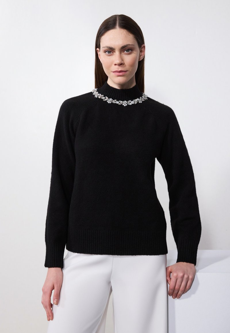 Schwarzer Wollpullover mit hohem Kragen und gerippten Bündchen, verziert mit einer dekorativen Kristall-Applikation am Kragen.