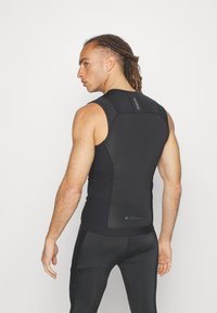 Black sleeveless performance top with a fitted design, textured panels, and logo details on the back. Worn with matching black leggings.
