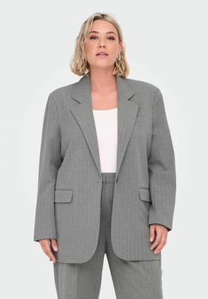 Šedý pruhovaný blazer s špičatým klopem a dvěma předními kapsami, nošený přes bílé tričko. Přiléhavý střih s uvolněnou siluetou.