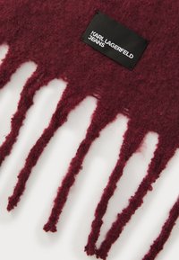 Bordo šal, pagamintas iš tekstūruotos vilnos, su pailgomis kutais. Prisegtas juodas etiketė su baltais užrašais "KARL LAGERFELD JEANS".