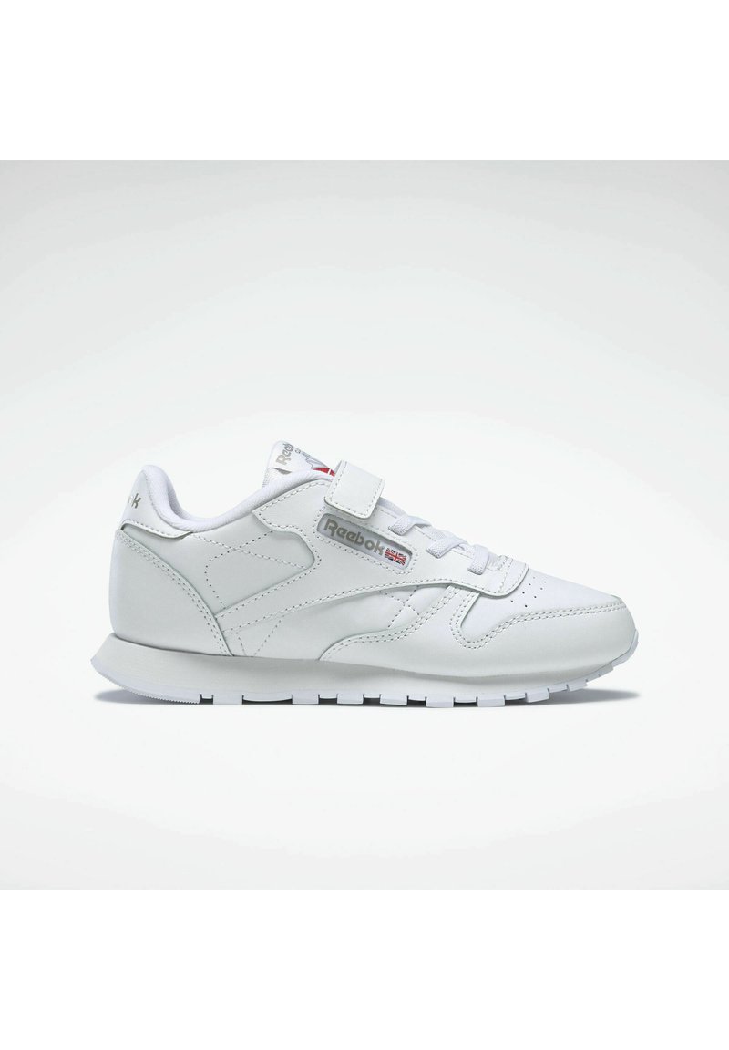 Zapatilla deportiva blanca con parte superior de cuero, parte frontal con cordones y tira de velcro. Presenta un cuello acolchado, paneles laterales texturizados y suela de goma.