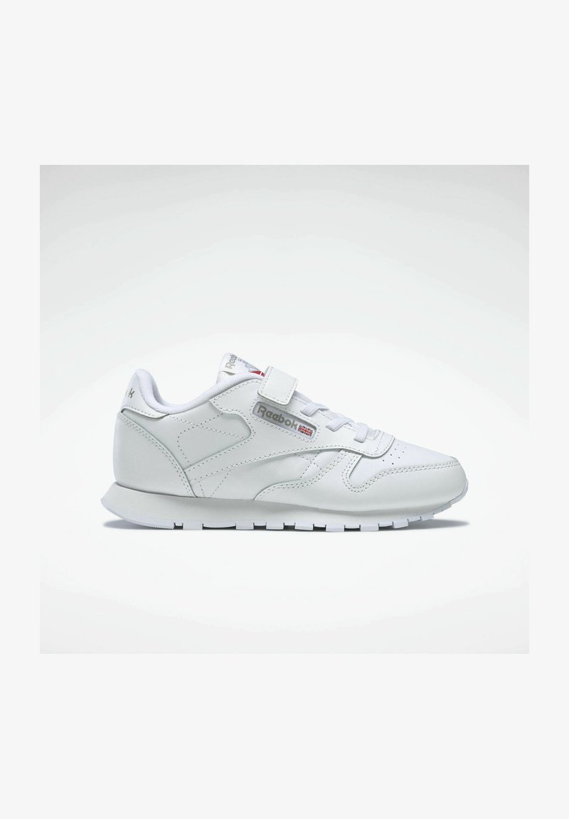 Vit träningsskor med överdel i läder, snörning framtill och kardborreband. Funktioner inkluderar en vadderad krage, texturerade sidopaneler och gummisula.