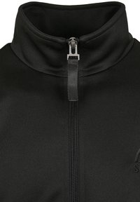 Veste zippée noire avec un col montant, fabriquée en tissu lisse et extensible ; dotée d'une fermeture éclair à l'avant et d'un logo sur la poitrine gauche.