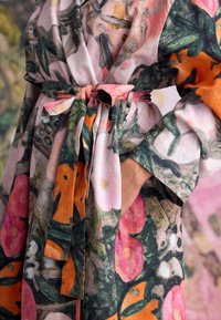 Wikkeljurk met bloemmotief van lichtgewicht stof in roze, oranje en groene tinten, met een strikceintuur en wijde mouwen.