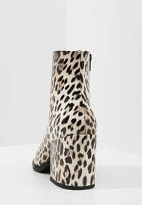 Stivale alla caviglia con stampa leopardo, finitura liscia, tacco a blocco e zip sul retro; presenta macchie nere su uno sfondo beige.