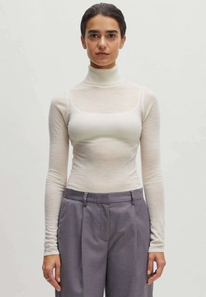 Witte, lange mouwen turtleneck top gemaakt van doorzichtige stof; aansluitende taille, ronde halslijn. Gecombineerd met grijze, hoge taille broeken met plooien.