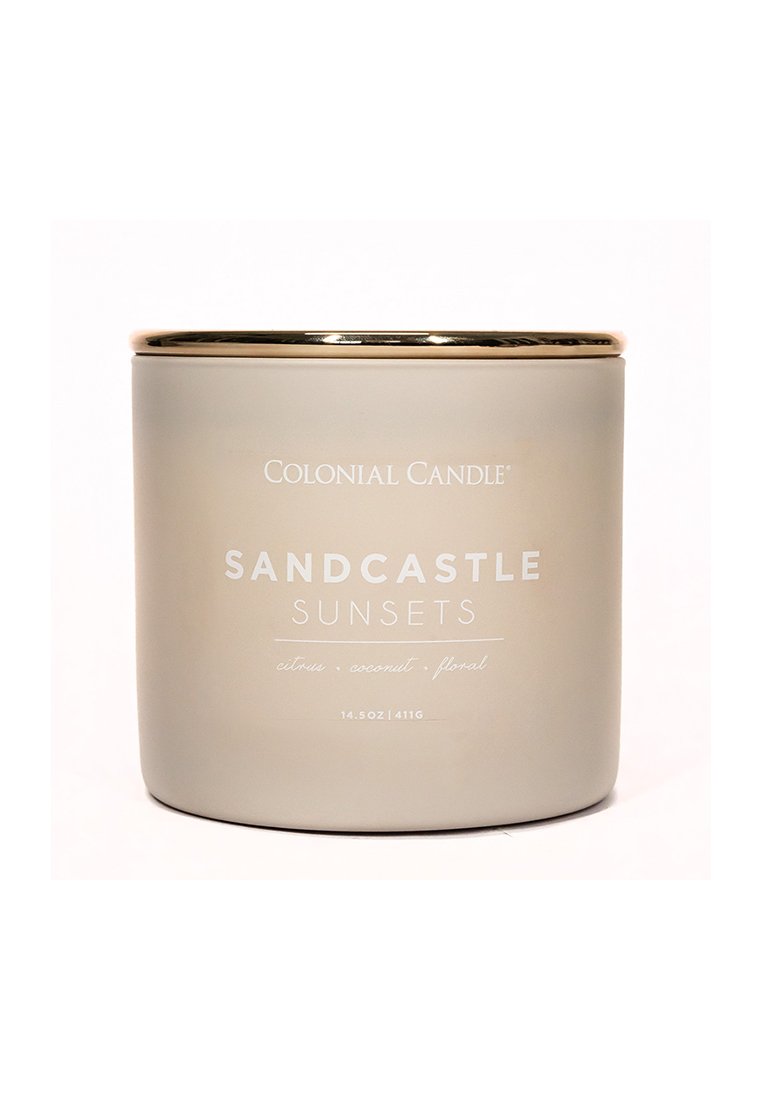 Ein zylindrischer, mattschimmernder Glasbehälter für Kerzen in mattem Beige, mit goldenen Akzenten und weißer Schrift, die "SANDCASTLE SUNSETS" liest.