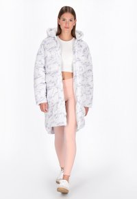 Puffer-Jacke in Weiß mit einem lila Marmor-Muster, ausgestattet mit Kapuze, langen Ärmeln und einem lockeren Schnitt, getragen über einem Cropped-Top und Leggings.