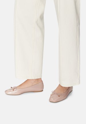 Pudrowo różowe baleriny z lakierowanej skóry, z zaokrąglonym noskiem, delikatną kokardką i płaską podeszwą, zestawione z jasnymi spodniami o szerokich nogawkach.