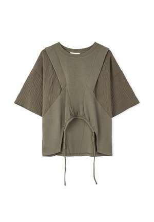 Maglietta oversize verde oliva con maniche corte, caratterizzata da dettagli a coste e una vita cinchata con lacci. Tessuto morbido e texture.