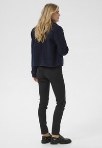 Veste texturée bleu marine avec une coupe décontractée, associée à un jean slim noir et des chaussures noires. Présente un col rond et des poignets à boutons.