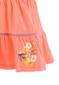 Korallfarbene Baumwollrock mit einem gestuften Design, das ein gelbes und weißes Blumenmuster sowie kontrastierende blaue Nähte am Saum aufweist.