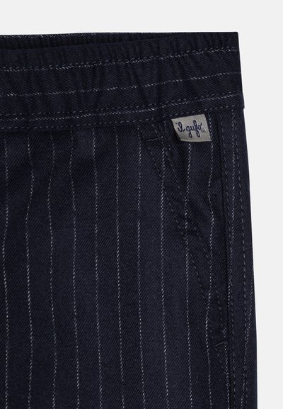 Tessuto di denim scuro con strisce verticali bianche, dotato di un morbido waistband e di una piccola etichetta grigia cucita nella cucitura laterale.