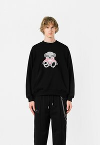 Sudadera negra con un gráfico de osito de peluche en gris y rosa. Hecha de material suave, con puños y dobladillo acanalados.