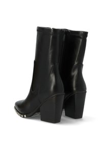 Botas de tobillo de cuero negro con un tacón alto y cuadrado y cremalleras laterales. Presentan una textura suave y un detalle metálico decorativo en la suela.