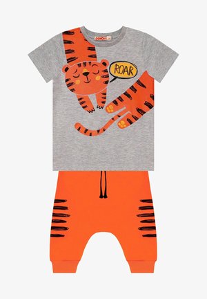 Šedé tričko s oranžovými grafikami tygra a bublinou s nápisem „ROAR“, spárované s oranžovými kalhotami s černými pruhy tygra a šňůrkou.