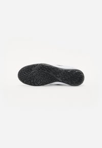 Semelle de chaussure en caoutchouc noir avec un motif de texture antidérapante et un talon arrondi, comportant un intercalaire blanc et un logo circulaire en relief.