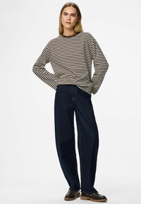 Žena sa ravnom plavom kosom nosi smešanja smeštenu dugom rukavu košulju smešnog smeštaja u smešnim smeškim smeškom.