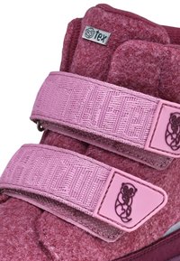 Roze vilt schoenen met twee brede klittenbandsluitingen. Heeft een textuurdesign en een klein reliëflogo van een aap op de strap.