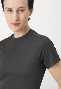 Camisa deportiva ajustada de color gris oscuro, con mangas cortas, tejido texturizado y detalles de costura sutiles en los hombros.