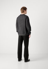 Mørkegrå, ribbestrikket genser med senkede skuldre, avslappet passform og svarte bukser. Ull-lignende tekstur og minimalistisk design.
